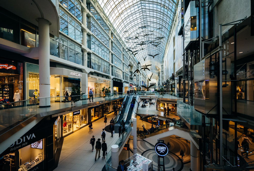 the inside of Toronto's Eatn Centre with people walking, escalators, shops and glass ceiling